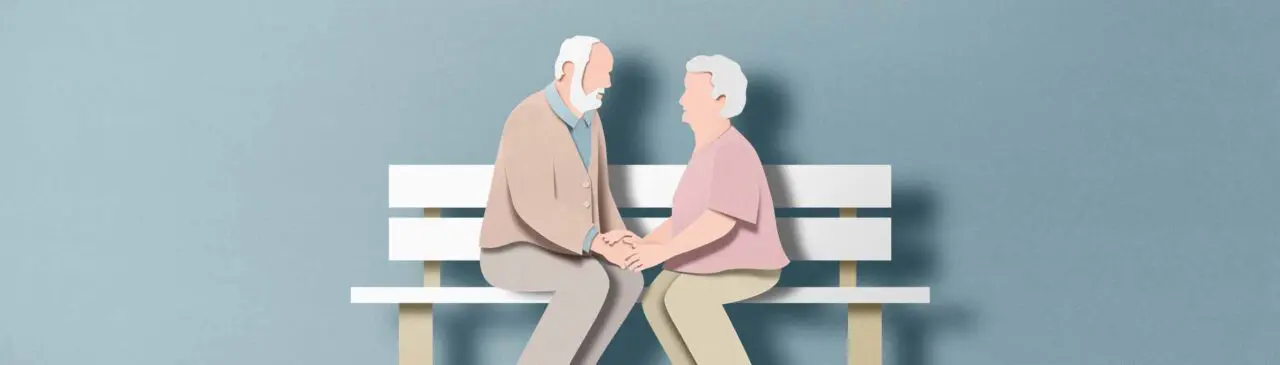 ältere Frau und älterer Mann sitzen auf einer Bank und halten sich an den Händen